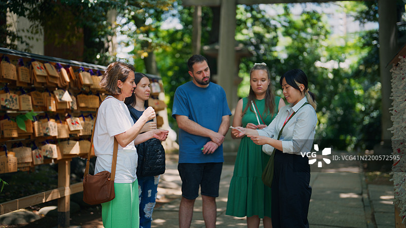 一位亚洲女性导游在日本神社为游客阅读和解释日本的签文（御御签）图片素材
