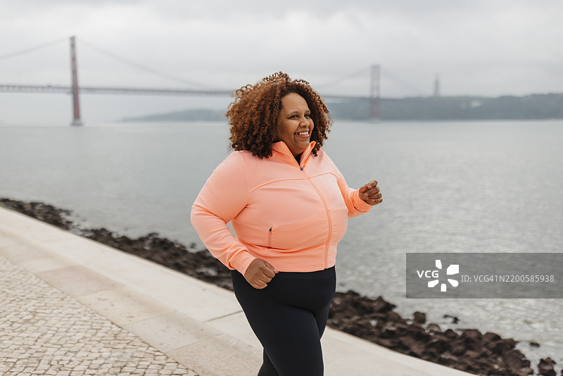 穿着鲜艳服装的女性在河岸边慢跑图片素材