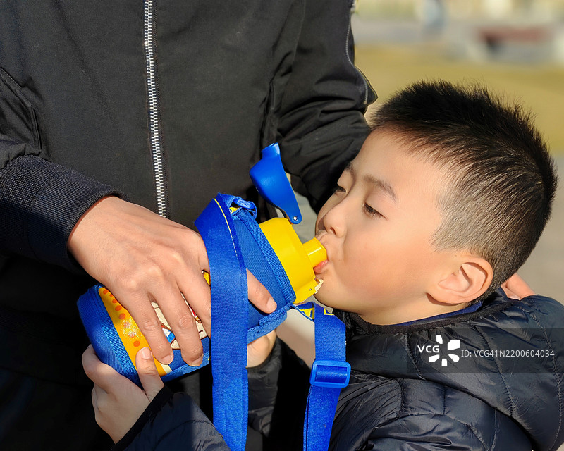 儿子口渴，父亲正在给他喝水。图片素材
