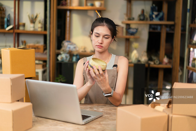女性工匠在笔记本电脑上管理陶器订单，旁边有箱子图片素材