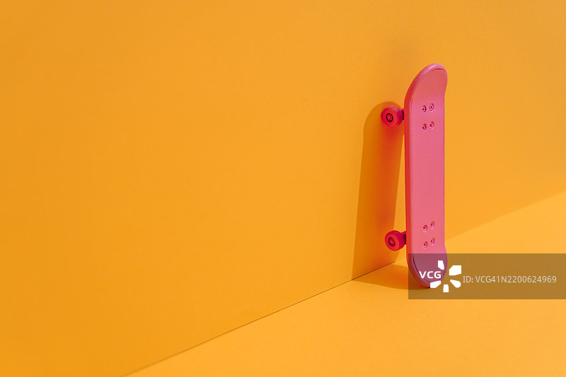 粉色滑板靠在黄色墙壁上，呈现极简风格的构图图片素材