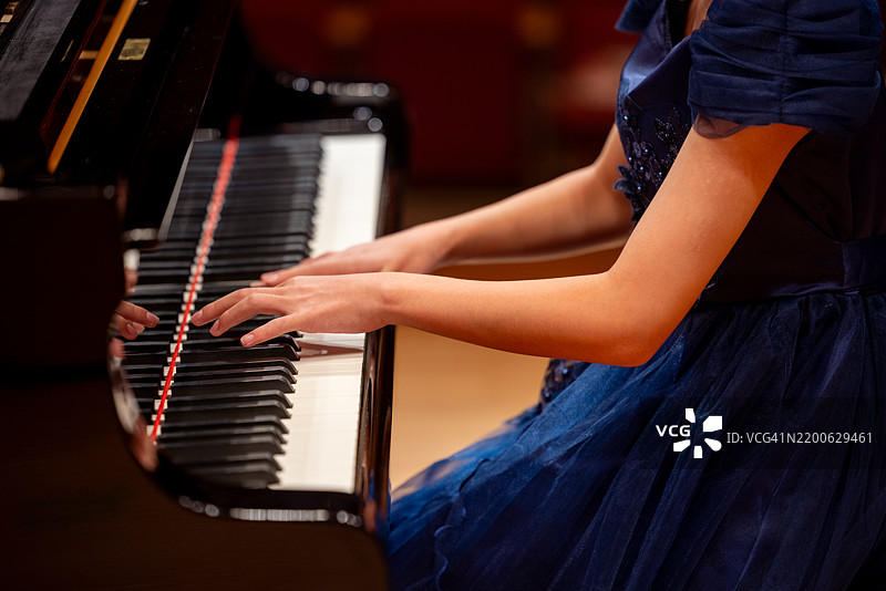 穿着蓝色裙子的少女手部特写，在音乐厅里弹钢琴图片素材