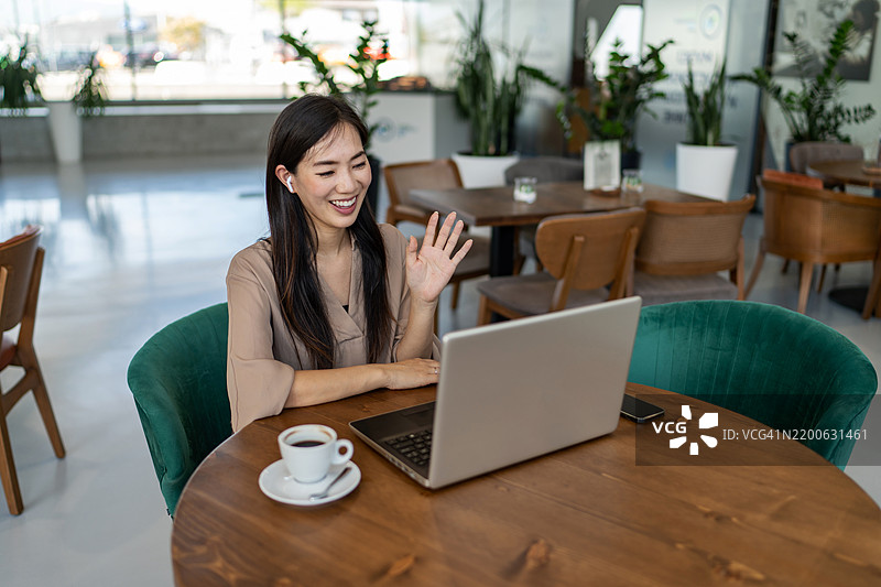 微笑的女商人坐在咖啡馆里通过视频通话与客户交谈图片素材