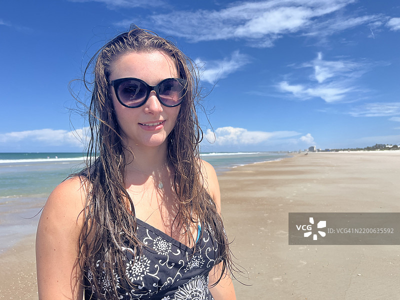 青少年在海滩上散步，享受家庭假期。女孩戴着太阳镜，穿着裙子。图片素材