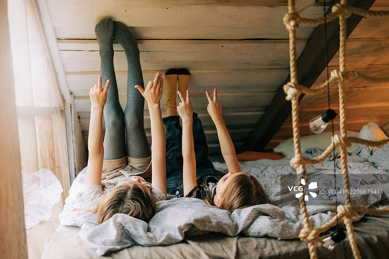 两个快乐的兄妹躺在床上，用手指做出顽皮的手势图片素材