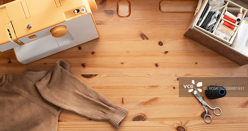 从上方俯瞰的裁缝桌，桌上有缝纫机、剪刀、线和衣物，横幅图像。图片素材