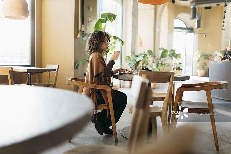 年轻女性在现代咖啡馆享受咖啡和糕点图片素材
