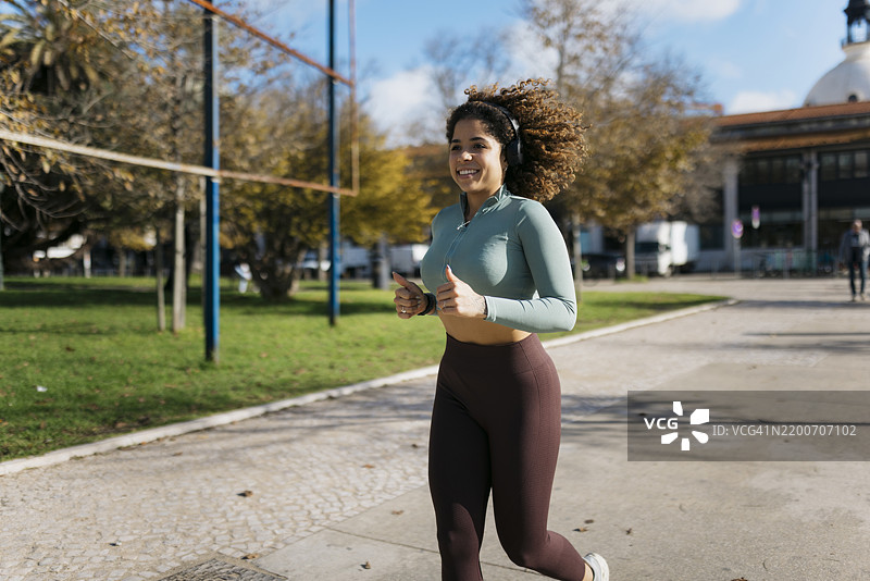 年轻女性在城市公园里跑步，佩戴耳机，穿着运动服图片素材