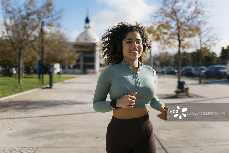 年轻女性在城市公园慢跑时戴着耳机微笑图片素材