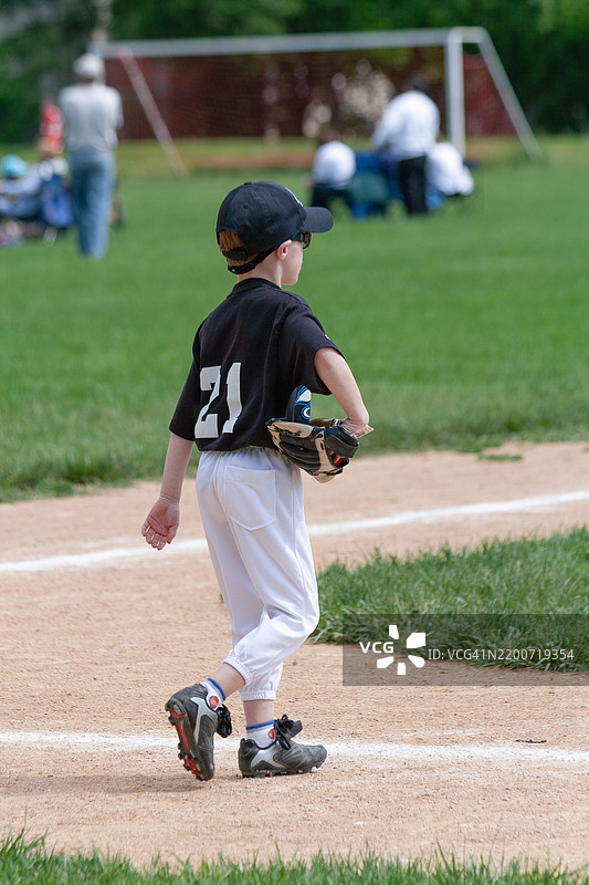 一个年轻男孩在他的球队完成击球后走向棒球场。图片素材