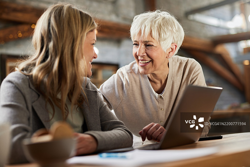 快乐的老年母亲和成年女儿在家中使用笔记本电脑。图片素材
