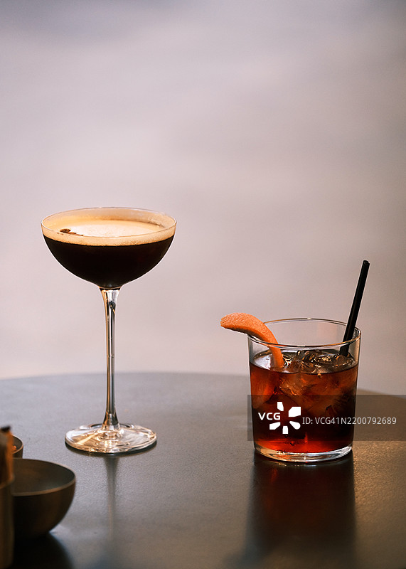 浓缩咖啡马提尼和尼格罗尼鸡尾酒在光滑的深色桌子上呈现，优雅的酒吧环境，精致的饮品展示，优质的调酒和高档饮酒理念图片素材
