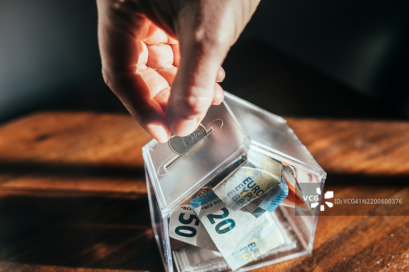 在家里把硬币放进一个像小房子的储蓄罐里。图片素材