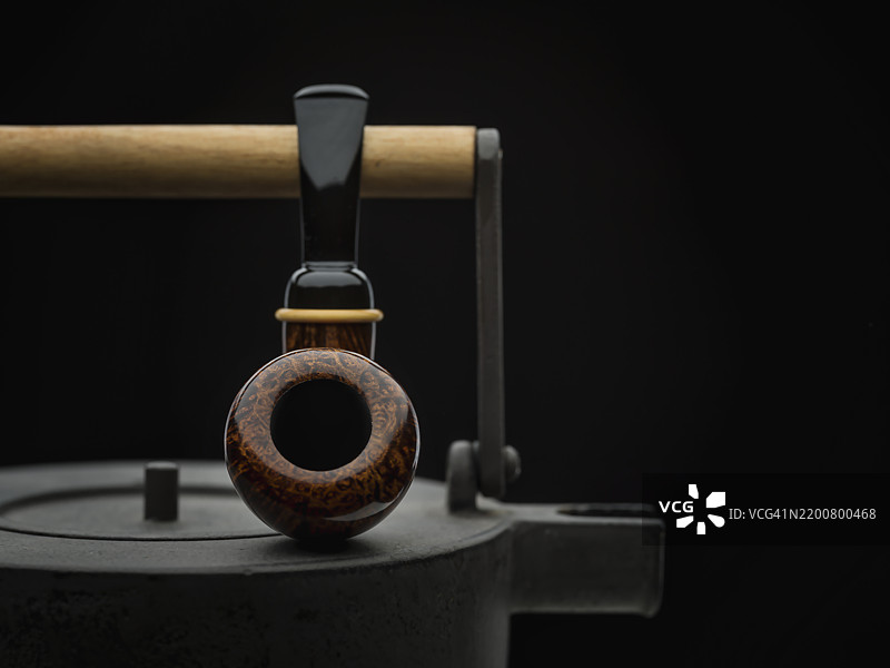 光滑的自由形状橡果烟斗放在复古金属茶壶上图片素材