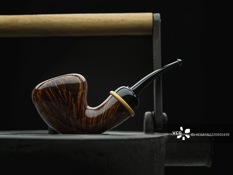 光滑的自由形状橡果烟斗放在复古金属茶壶上图片素材