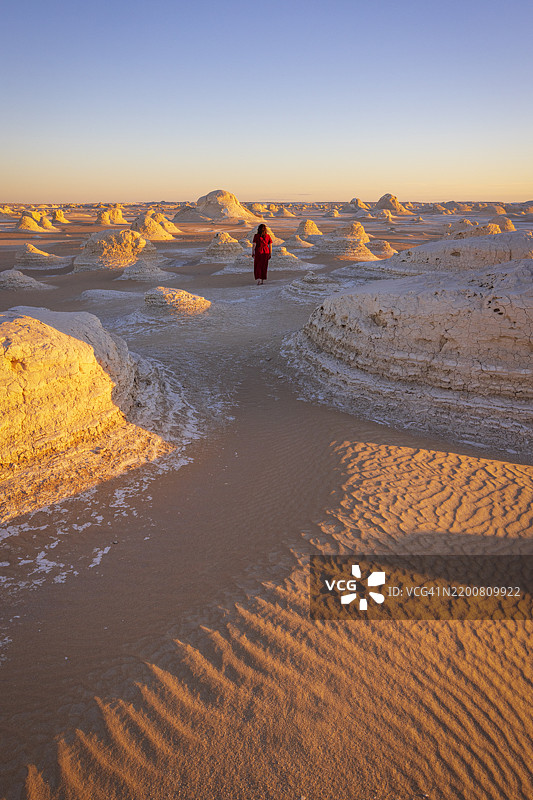 一位女性在埃及非洲白沙漠美丽的岩石 formations 附近散步，享受着美丽的日出。图片素材