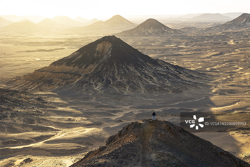 一个男孩在埃及非洲的黑色沙漠中的古老火山上欣赏美丽的日落。图片素材