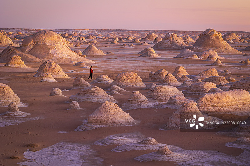 一位女性在埃及非洲白沙漠美丽的岩石 formations 附近散步，背景是迷人的日落。图片素材