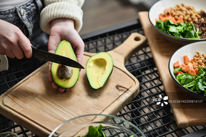 女性用厨房刀去除鳄梨种子，然后将其加入佛碗中图片素材