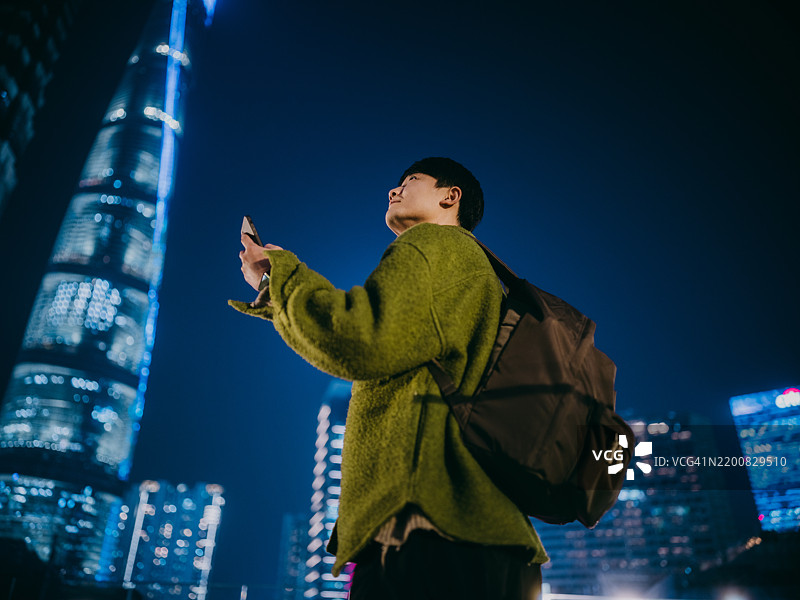 自信的亚洲男子在上海金融区的高楼大厦间使用智能手机图片素材