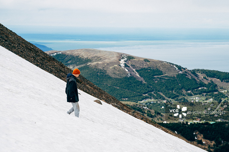 阿拉斯加一名少年男孩在雪-covered陡峭山坡上徒步旅行图片素材