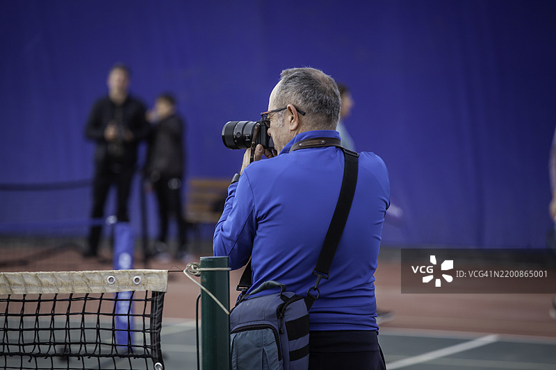 男性摄影师在硬地球场上拍摄乒乓球照片，横向静态。图片素材