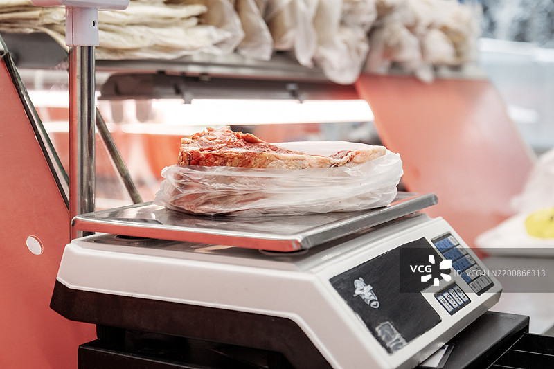 数字秤上称重的肉类。肉店中装在塑料袋里的生牛排部分图片素材