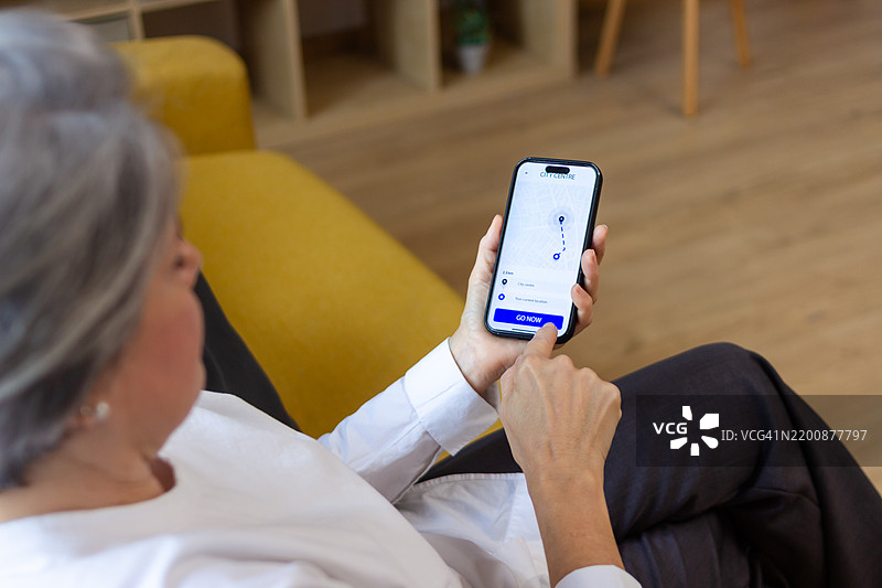 老年女性在家中使用汽车共享应用程序的智能手机图片素材