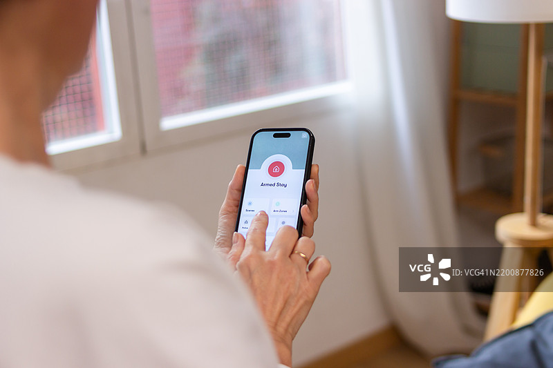 女性使用智能手机上的移动应用程序设置家庭安全系统图片素材