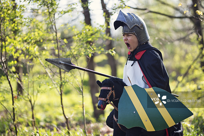 年轻男孩穿着中世纪骑士服装，在森林里骑着玩具马图片素材