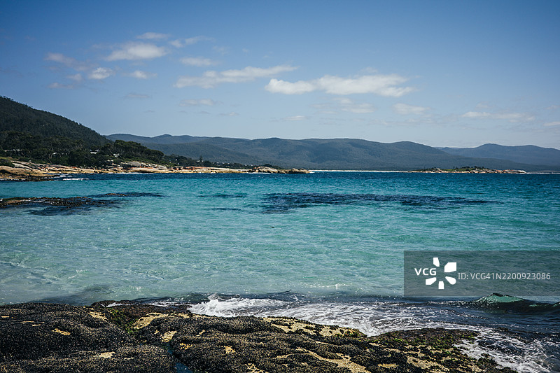 美丽的海滩景色，岸边有岩石，蓝天和清澈的水。图片素材