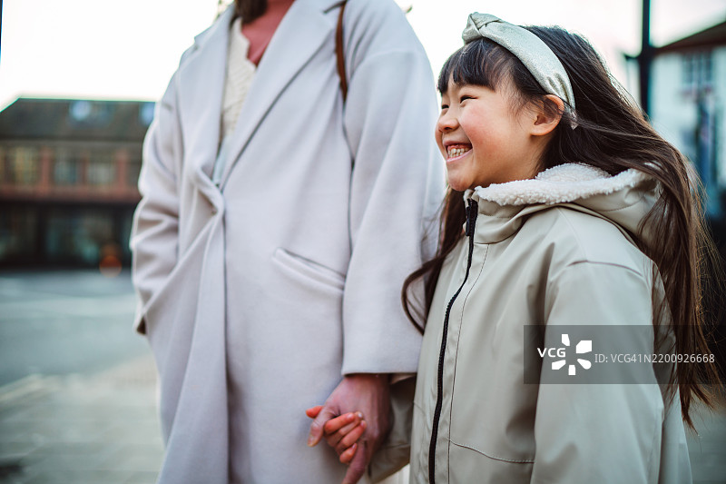 快乐的小女孩和她的母亲在城市街道上散步，探索周围的环境图片素材