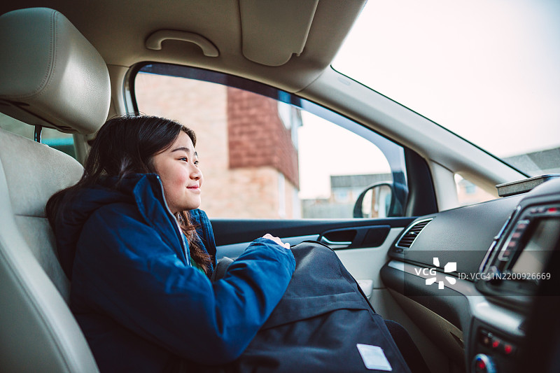 快乐的穿着校服的少女坐在前排乘客座位上，早晨乘车去学校。图片素材