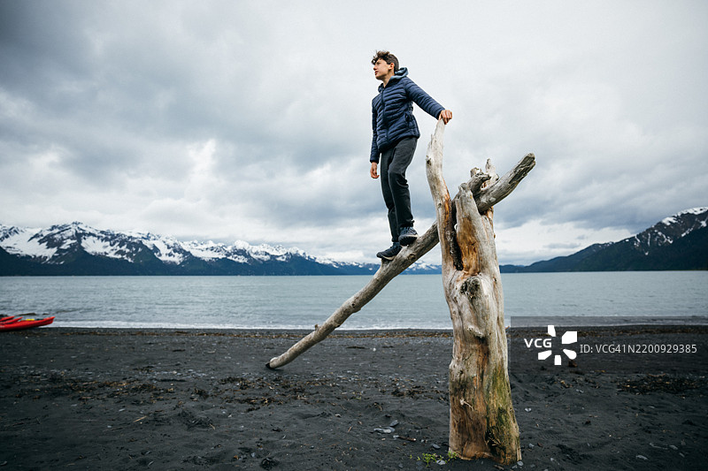 少年男孩在海滩的漂流木上俯瞰阿拉斯加的风景。图片素材