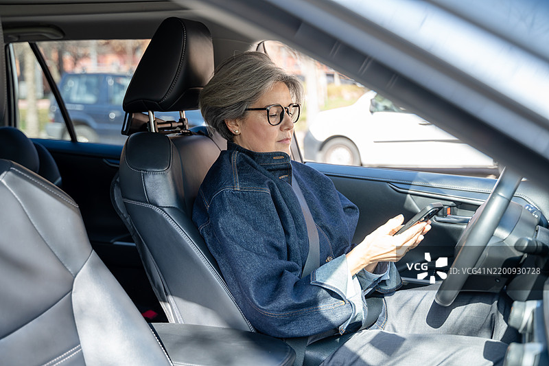 成熟的女商人在开车时使用智能手机图片素材