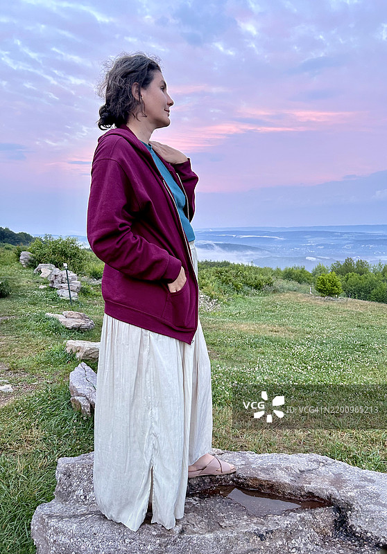 山脉在宾夕法尼亚州的山谷上投下长长的阴影，独自旅行者在石头平台上观望。粉紫色的日落照亮了靠近历史悠久的吉姆·索普地区的观景点。图片素材