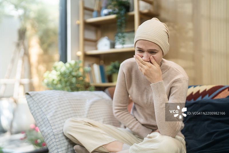 一位正在哀悼的癌症患者坐在安静的房间里，穿着米色毛衣和帽子。图片素材
