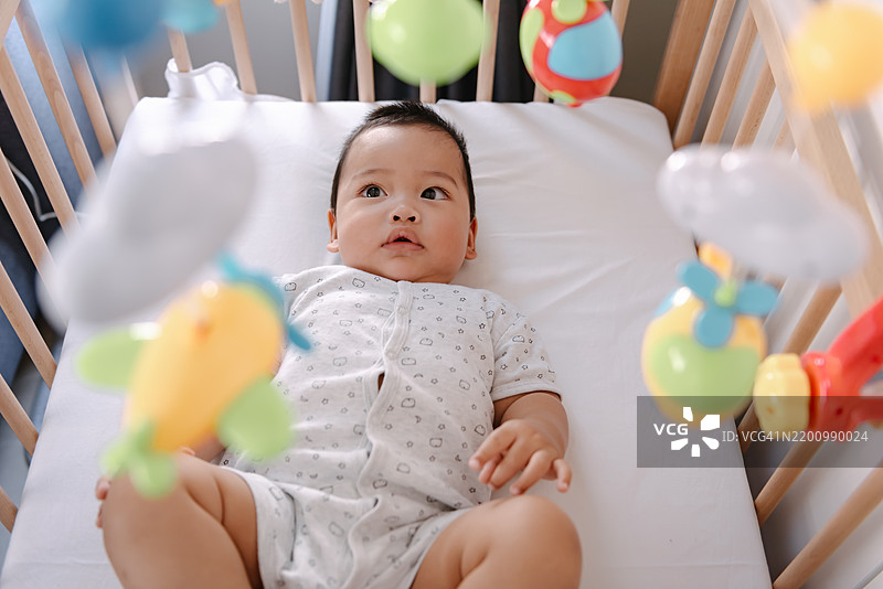 高角度视图下，婴儿男孩在婴儿床上玩悬挂的移动玩具。图片素材