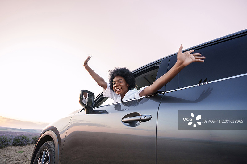 微笑的女性双臂伸展，倾身出车窗，仰望天空图片素材