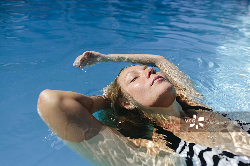 女人在游泳池中闭眼漂浮在水面上图片素材