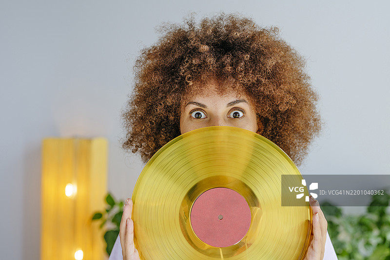 年轻的卷发女性凝视着并握着唱片播放器图片素材