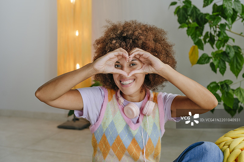微笑的年轻女性在家中做出心形手势图片素材