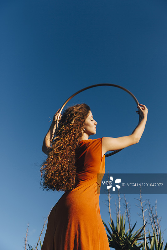 年轻的芭蕾舞艺术家在蓝天之下闭眼站立，手中握着塑料圈。图片素材