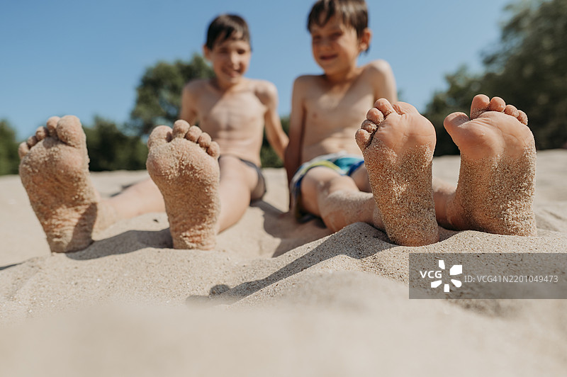 快乐的兄弟姐妹展示被沙子覆盖的脚丫图片素材