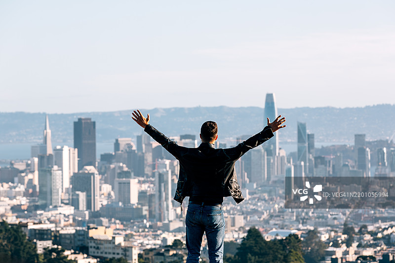 一名男子背对镜头，双臂张开，俯瞰加利福尼亚州旧金山的城市景观。图片素材