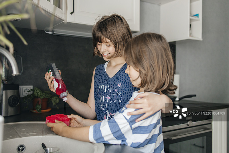 温柔的女孩在厨房里倒洗洁精，帮助哥哥。图片素材