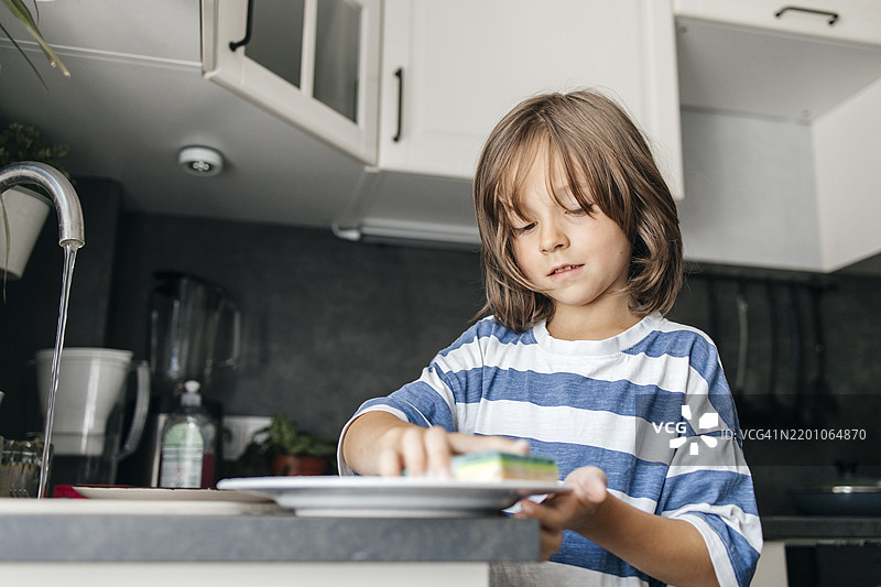 男孩在厨房水槽旁洗碗图片素材