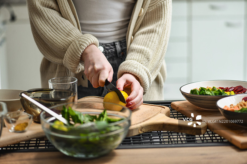 女性将柠檬切成两半，准备清淡健康的沙拉酱。图片素材