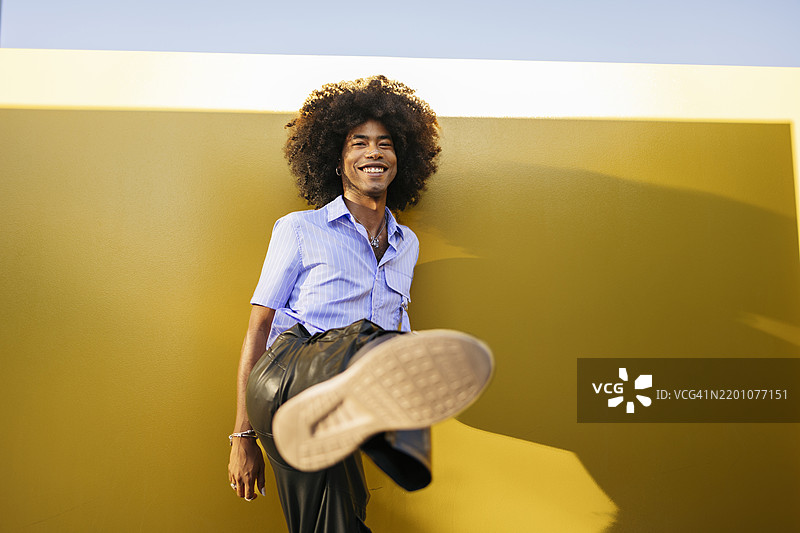 微笑的年轻男子在黄色墙壁旁展示鞋底图片素材