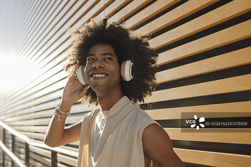 微笑的年轻男子在条纹墙旁通过无线耳机听音乐图片素材